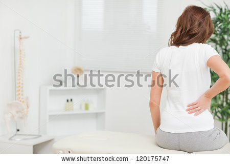 stock-photo-woman-sitting-on-a-table-while-touching-her-back-in-a-medical-room-120175747
